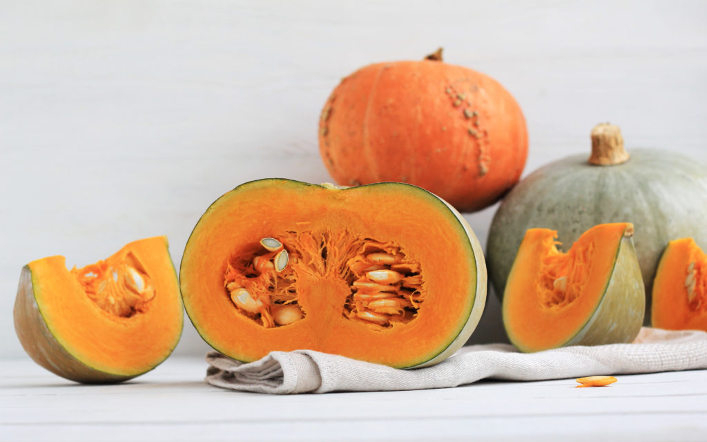 Group of halves and whole pumpkin on a light wooden background. Pumpkin is not cleared of seeds. Place for text.