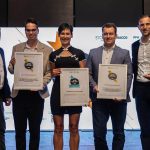 Five people holding awards in front of a screen, celebrating their achievements.